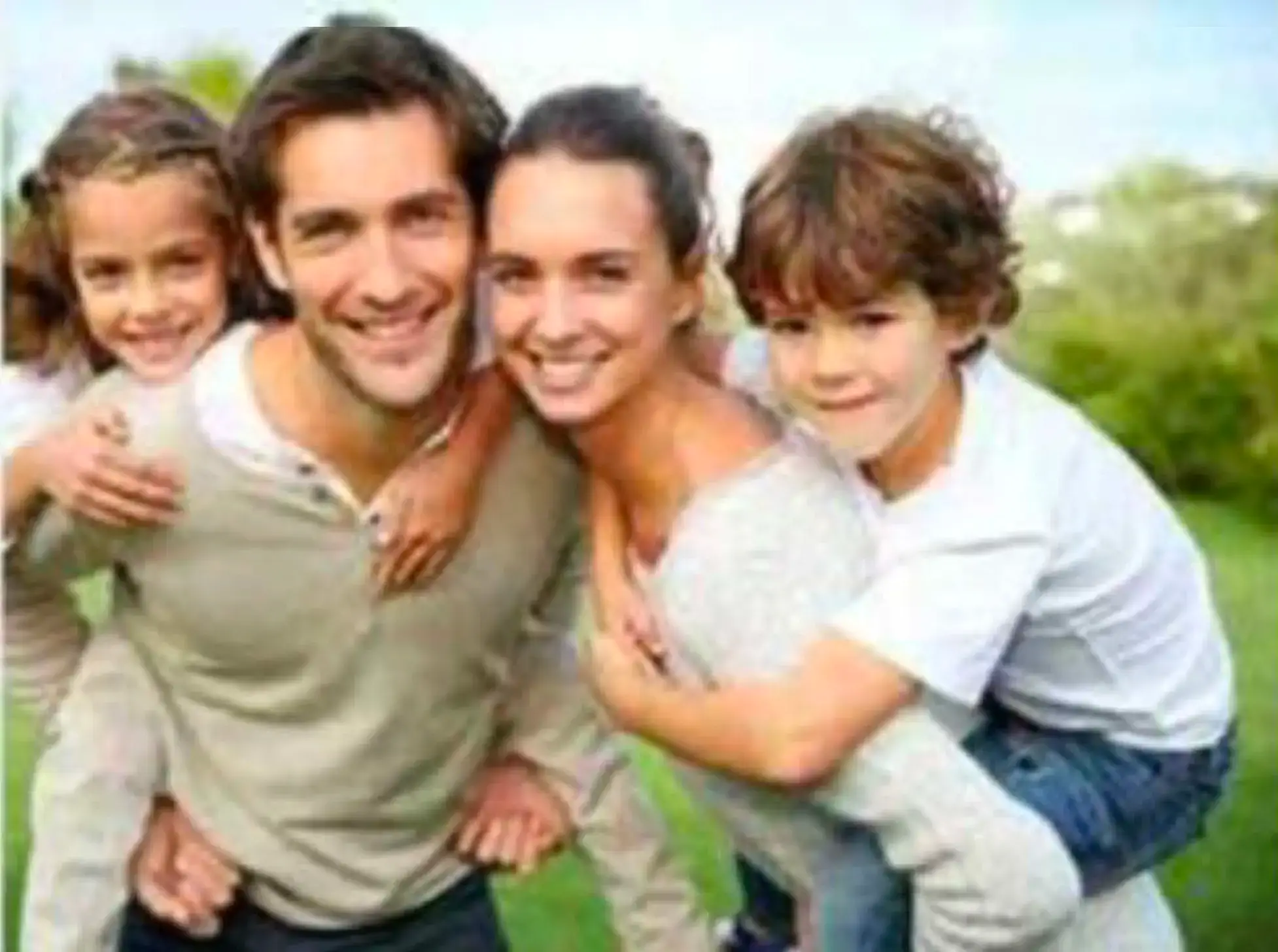 Smiling family of four outdoors, with two children on their parents' backs, representing healthy vision and family eye care.